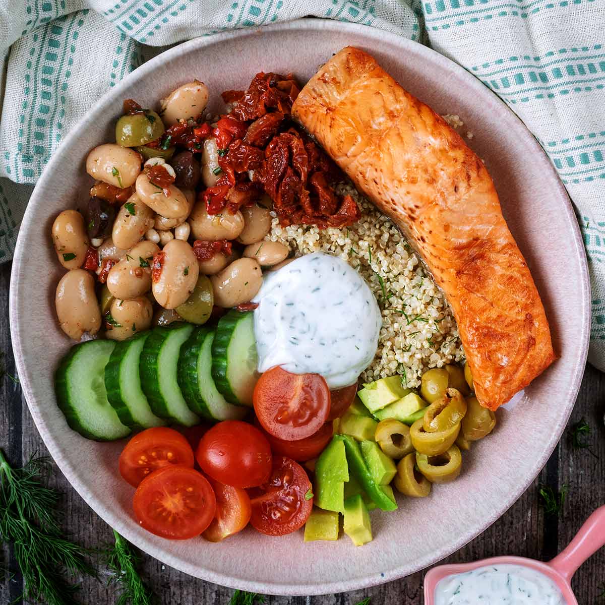A salmon quinoa bowl with salad vegetables, beans and a creamy dressing.