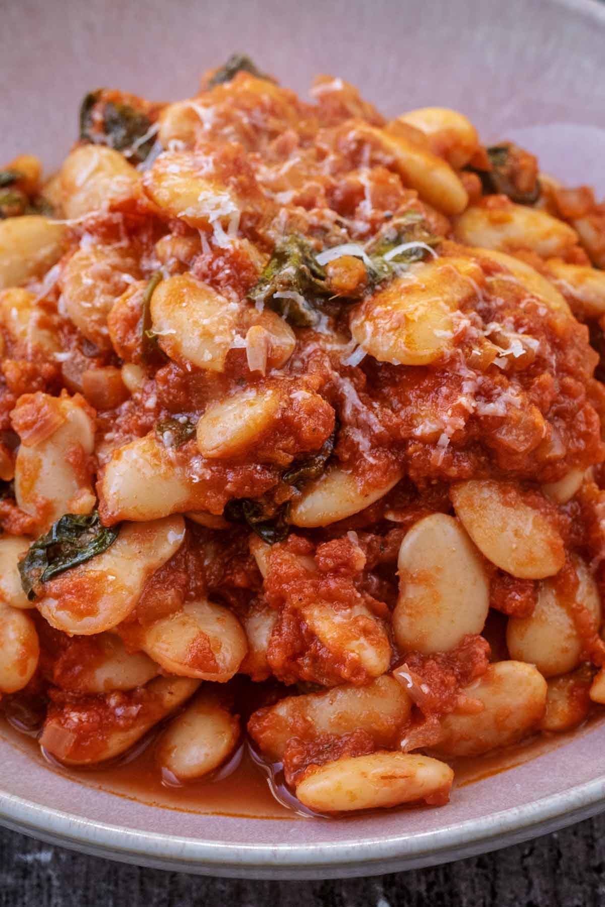 Butter beans in a tomato sauce in a pink bowl.