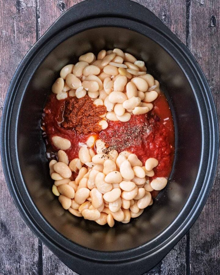 Chopped tomatoes, butter beans, pesto and seasoning in a slow cooker bowl.