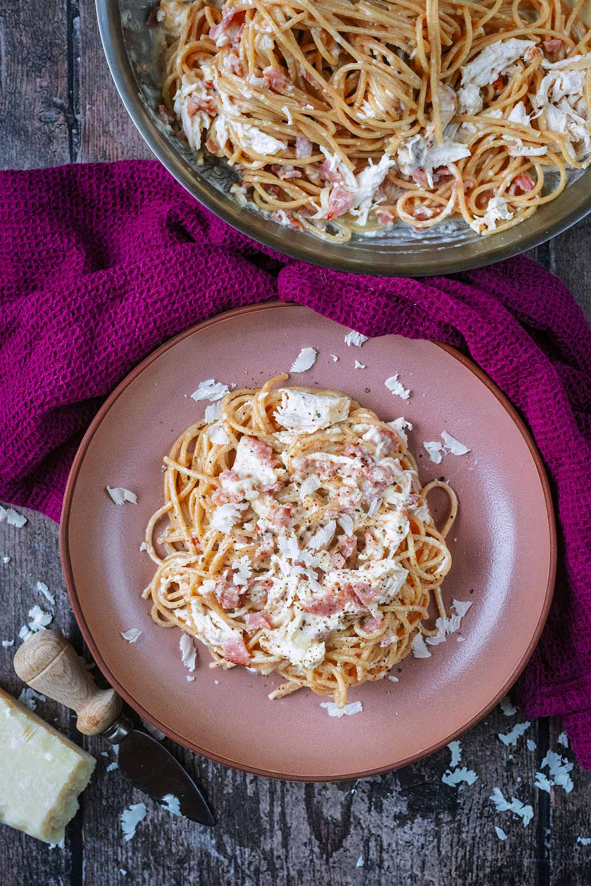 A bowl of spaghetti carbonara next to a pan of more carbonara.