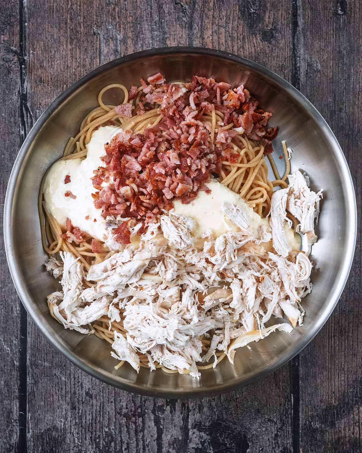 Cooked spaghetti, chopped bacon, shredded chicken and carbonara sauce in a large pan.