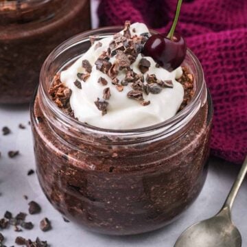 A glass jar full of chocolate cherry overnight oats, topped with a fresh cherry.