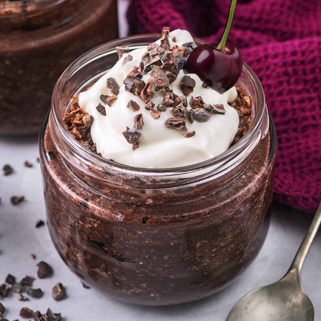 A glass jar full of chocolate cherry overnight oats, topped with a fresh cherry.