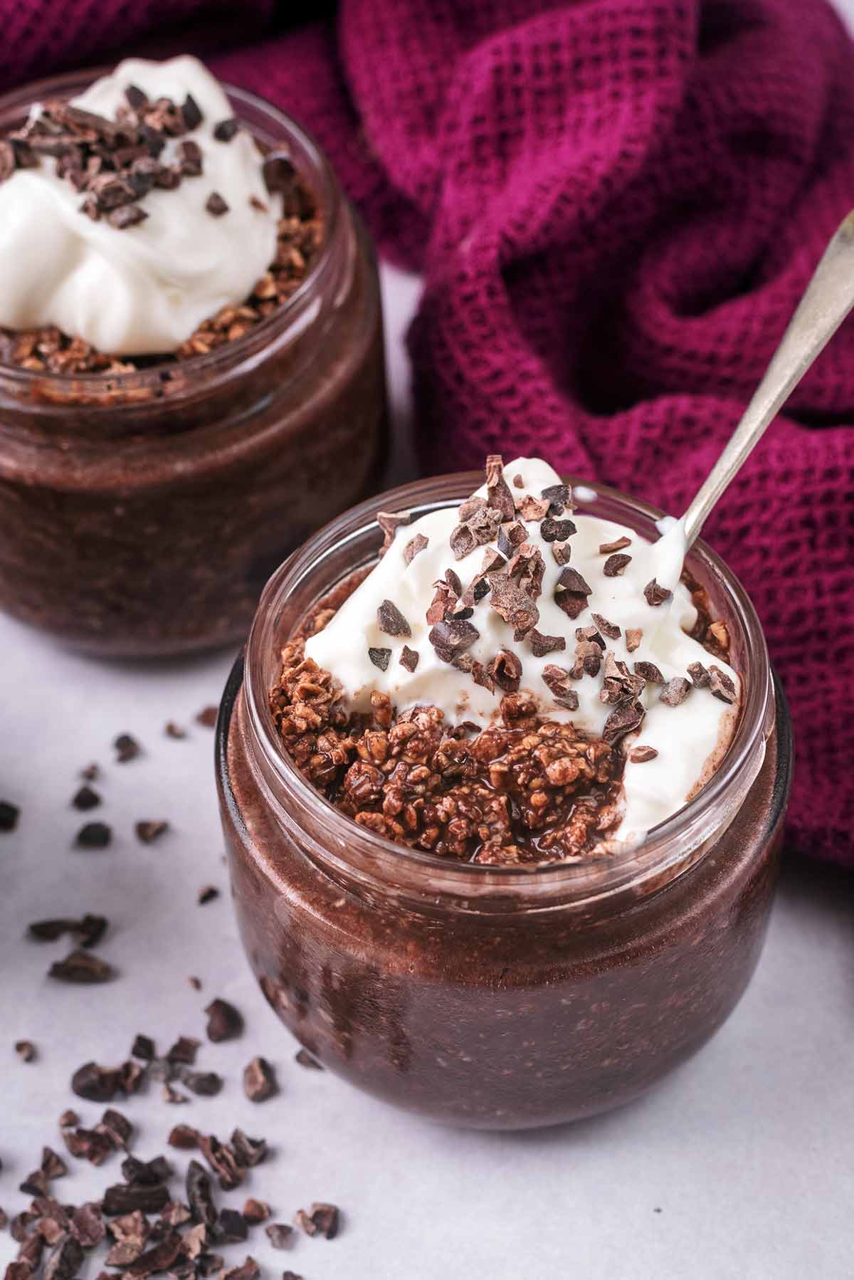 Two jars of chocolate overnight oats, one with a spoon in.