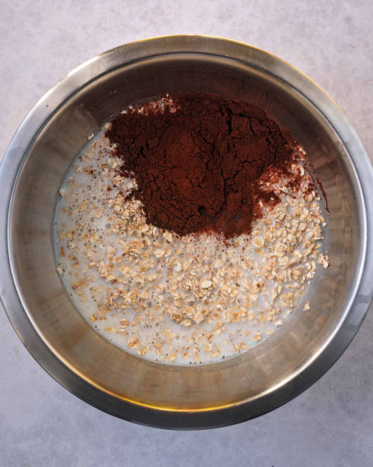 A mixing bowl containing oats, milk and cocoa powder.