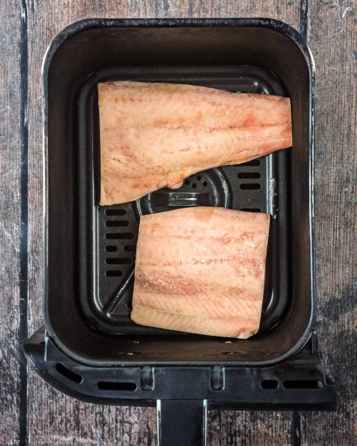 Two salmon fillets in an air fryer basket.