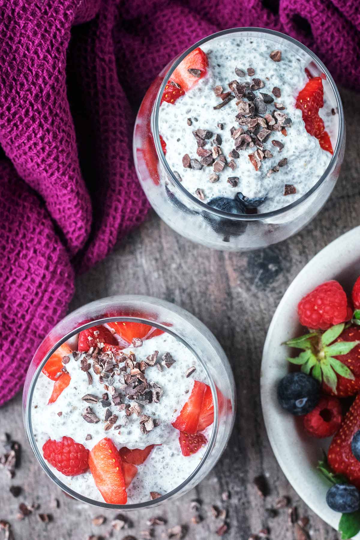 Two glasses of chia pudding topped with cacao nibs as viewed from above.