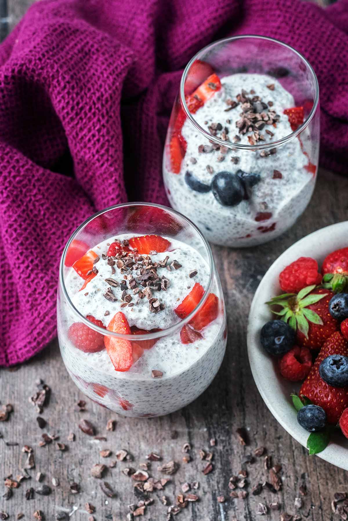 glasses of chia pudding next to a bowl of mixed berries.