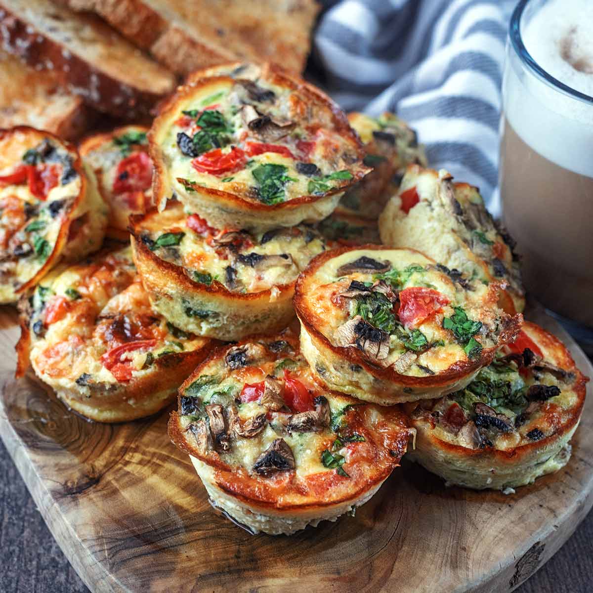 Ten cottage cheese egg bites piled up on a wooden board.