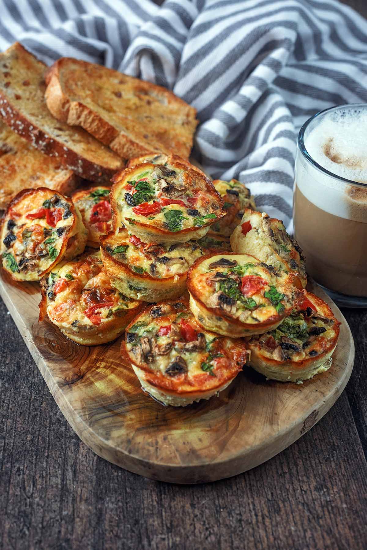 A pile of egg bites and some slices of toast on a wooden board.