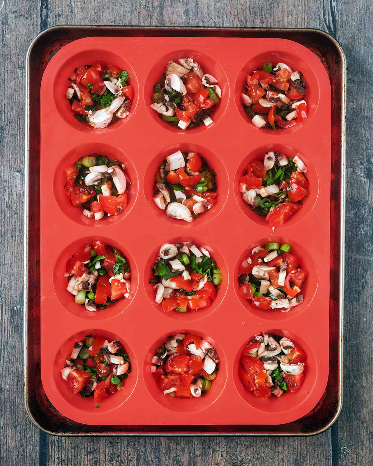 A twelve hole silicone muffin tray with chopped vegetable in each hole.