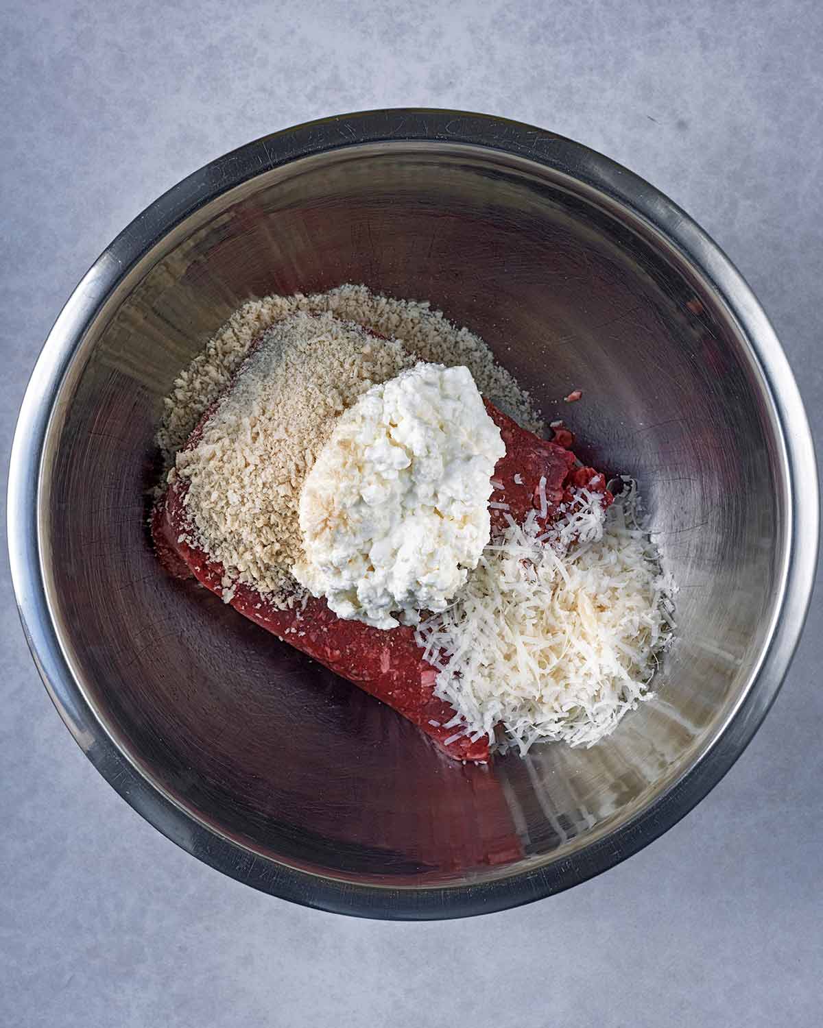 A mixing bowl containing beef mince, cottage cheese, Parmesan, breadcrumbs and seasoning.