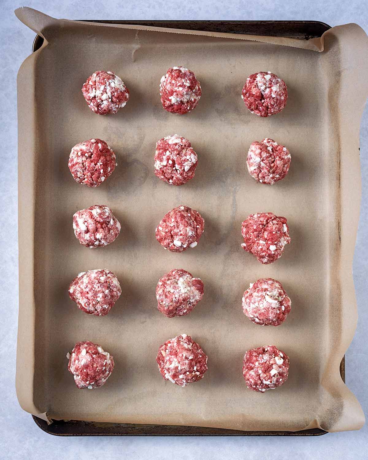 Fifteen uncooked meatballs on a lined baking tray.