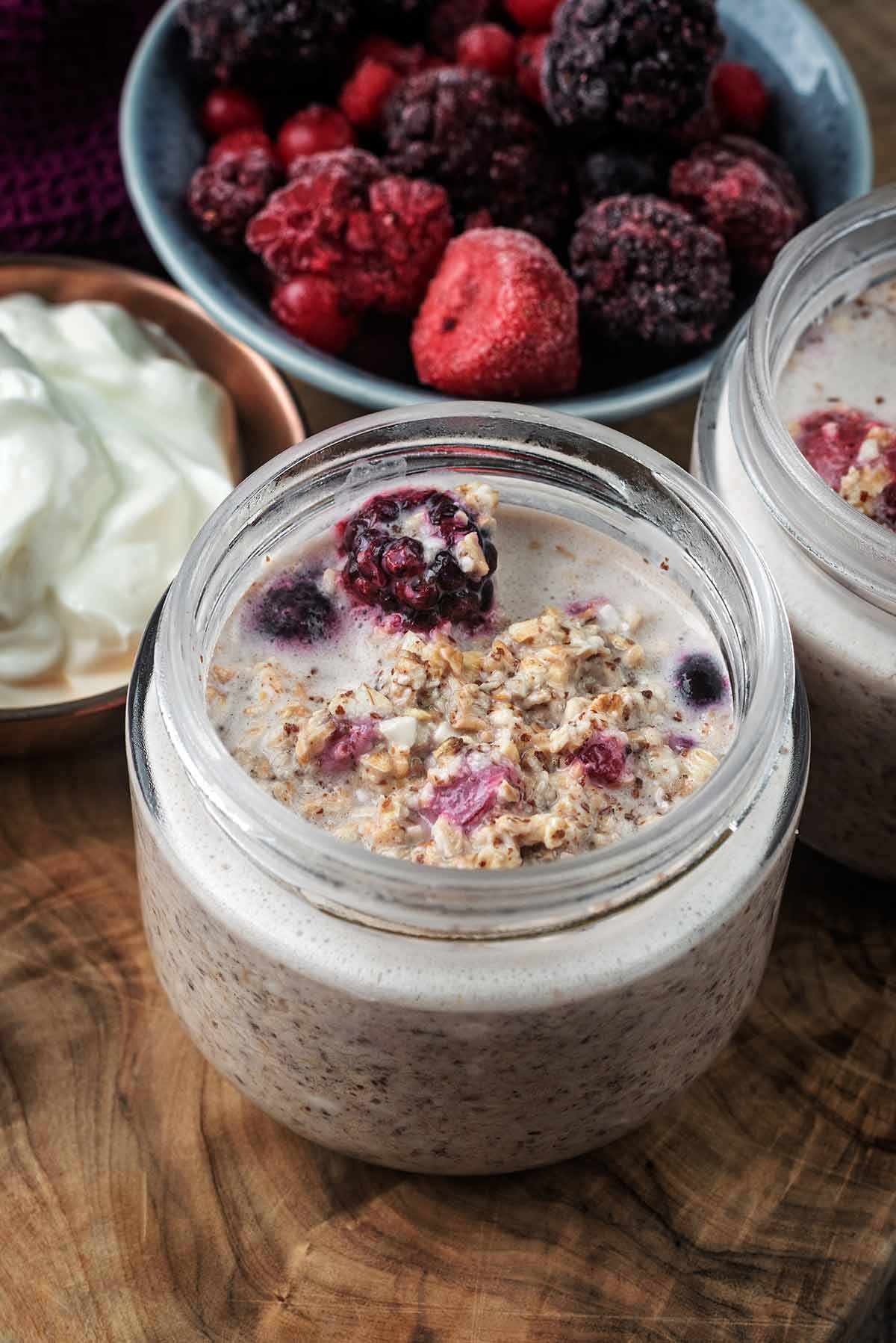 A jar of overnight oats in front of a bowl of berries.