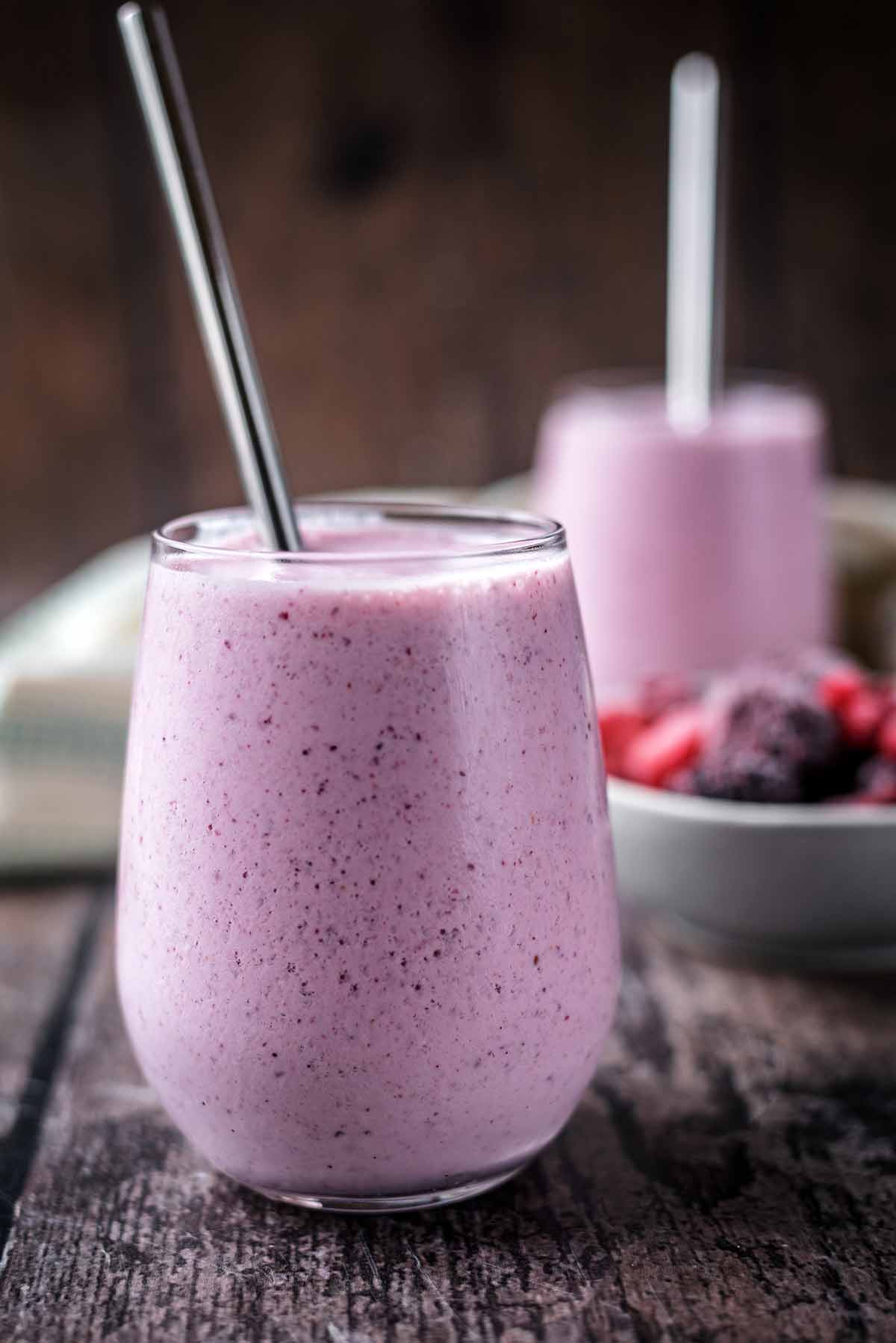 A glass of vibrant pink smoothie with another smoothie in the background.