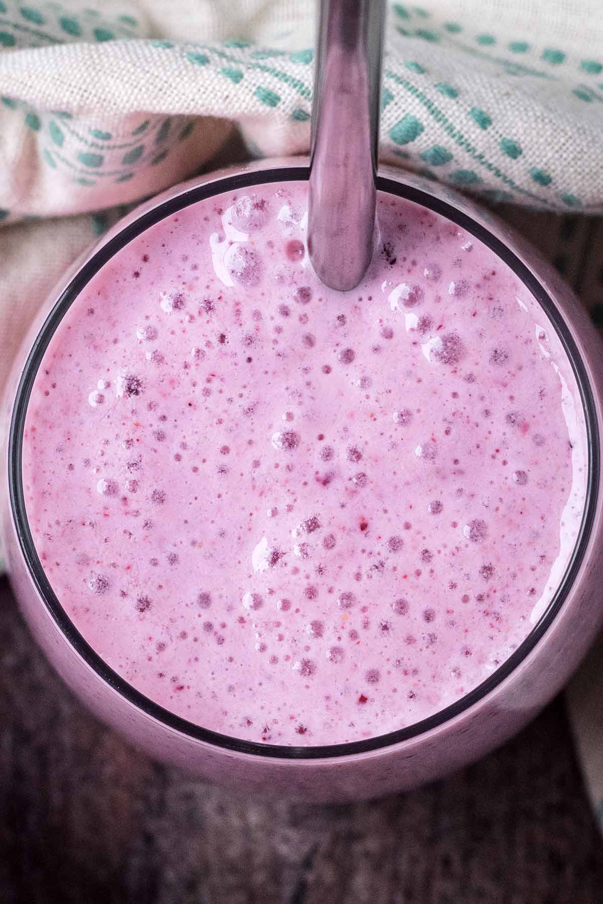 A pink smoothie in a glass with a metal straw as viewed from above.