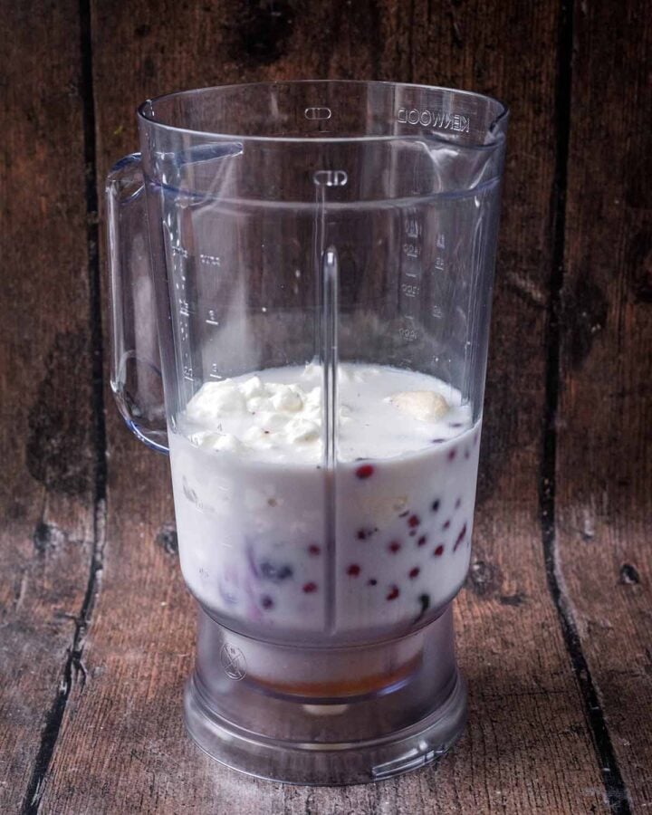 A blender jug containing cottage cheese, milk and berries.