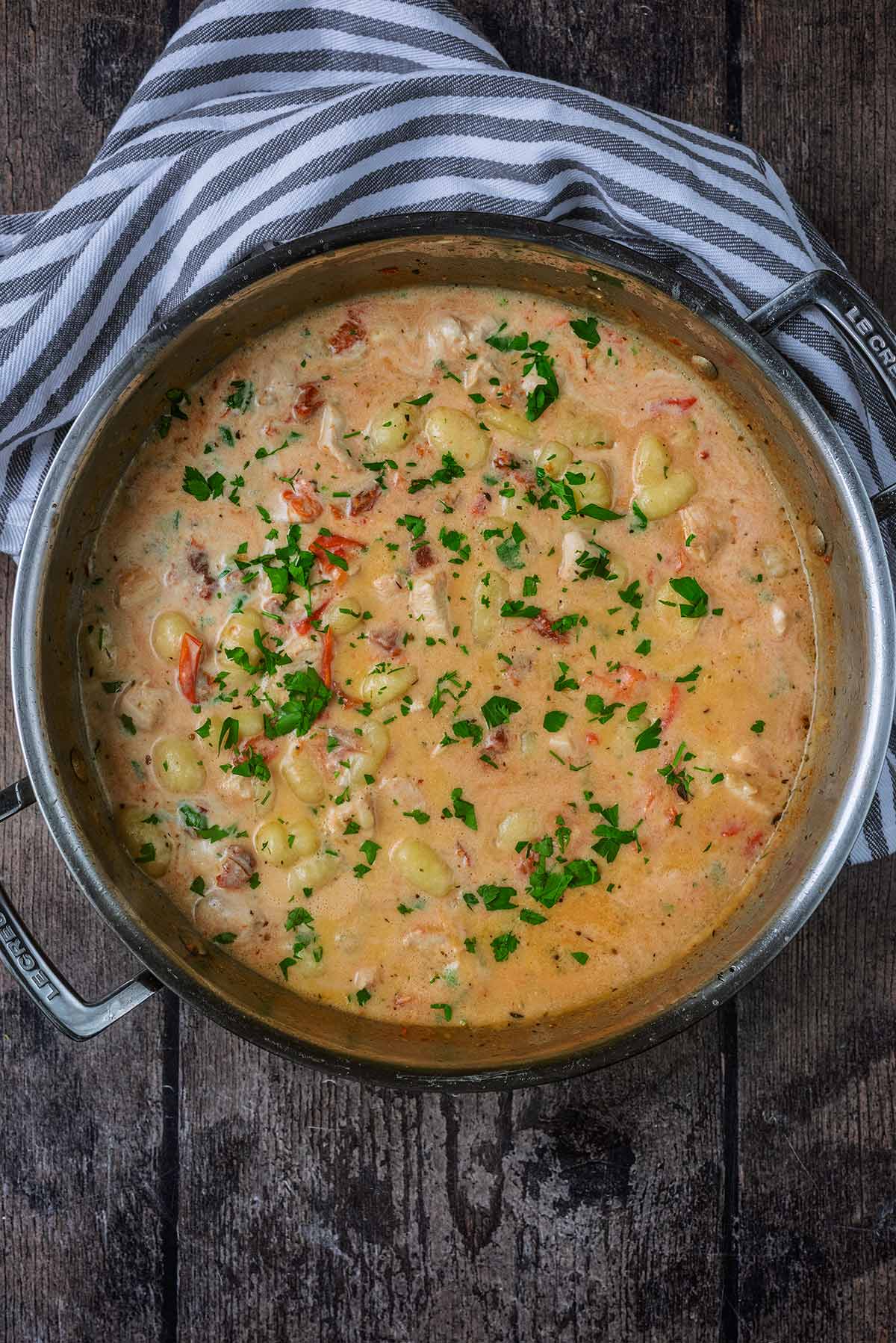 Creamy chicken gnocchi in a pan next to a striped towel.