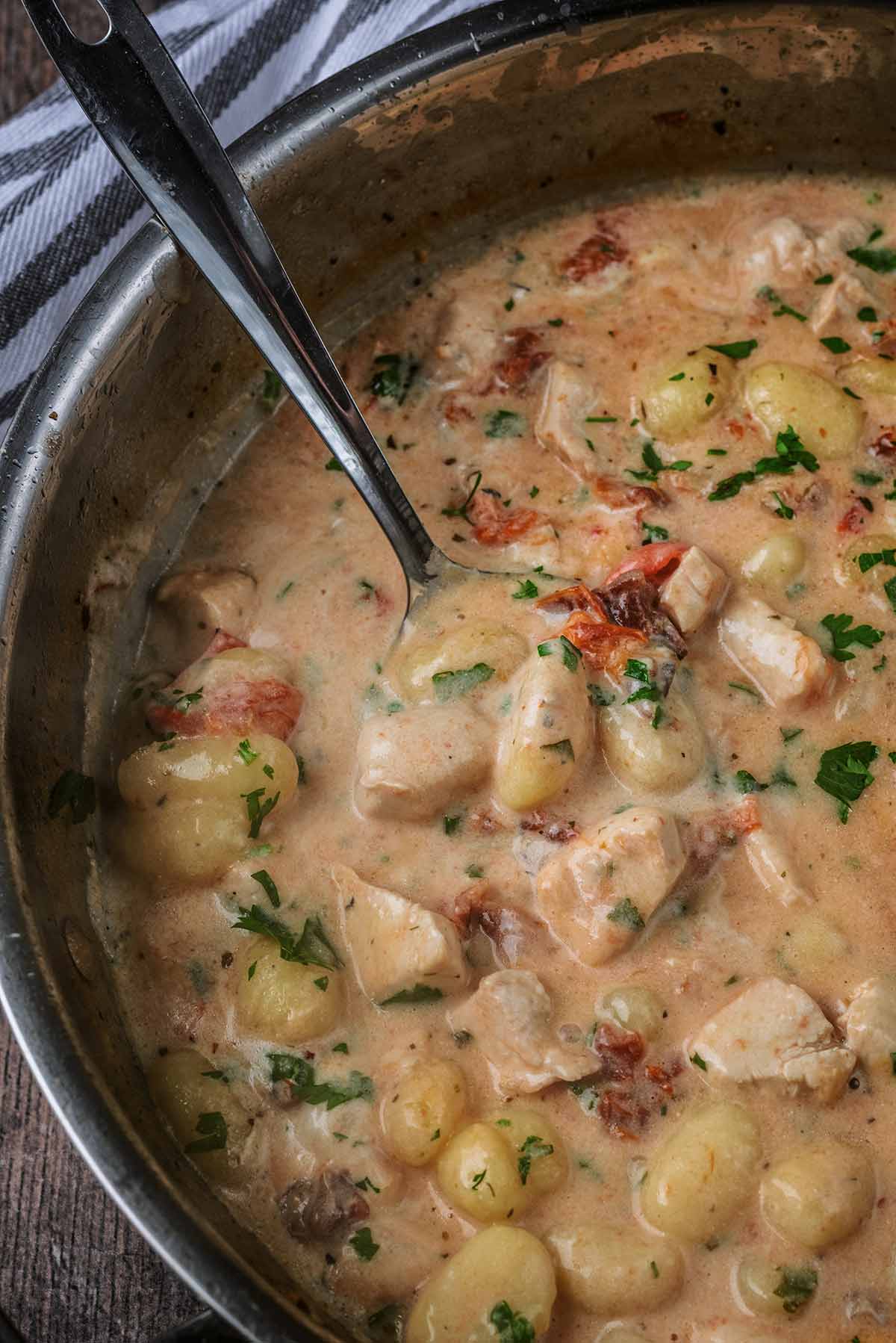 A large pan full of a creamy chicken gnocchi with a spoon in it.