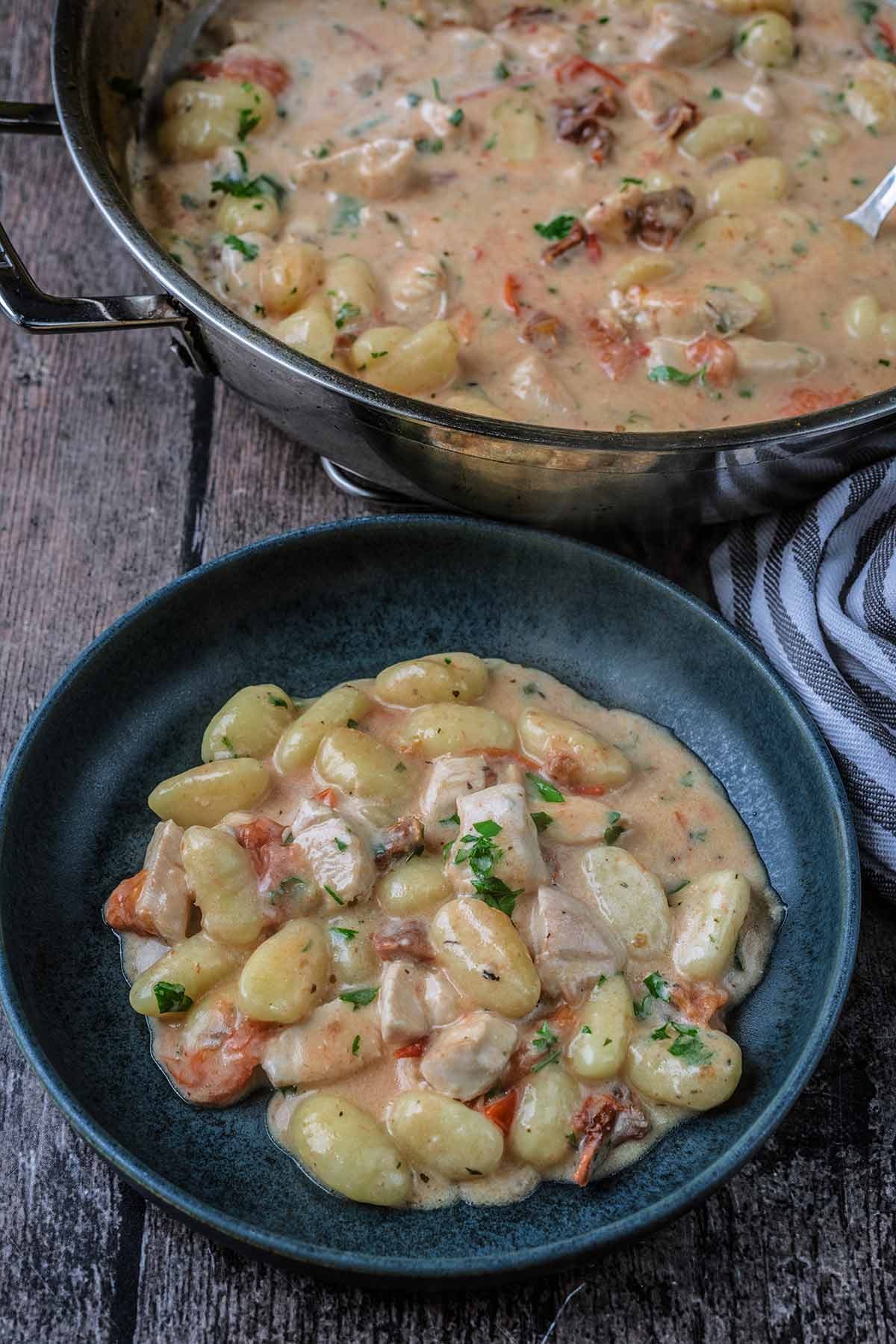 A bowl of creamy chicken gnocchi in front of a pan of more of the dish.