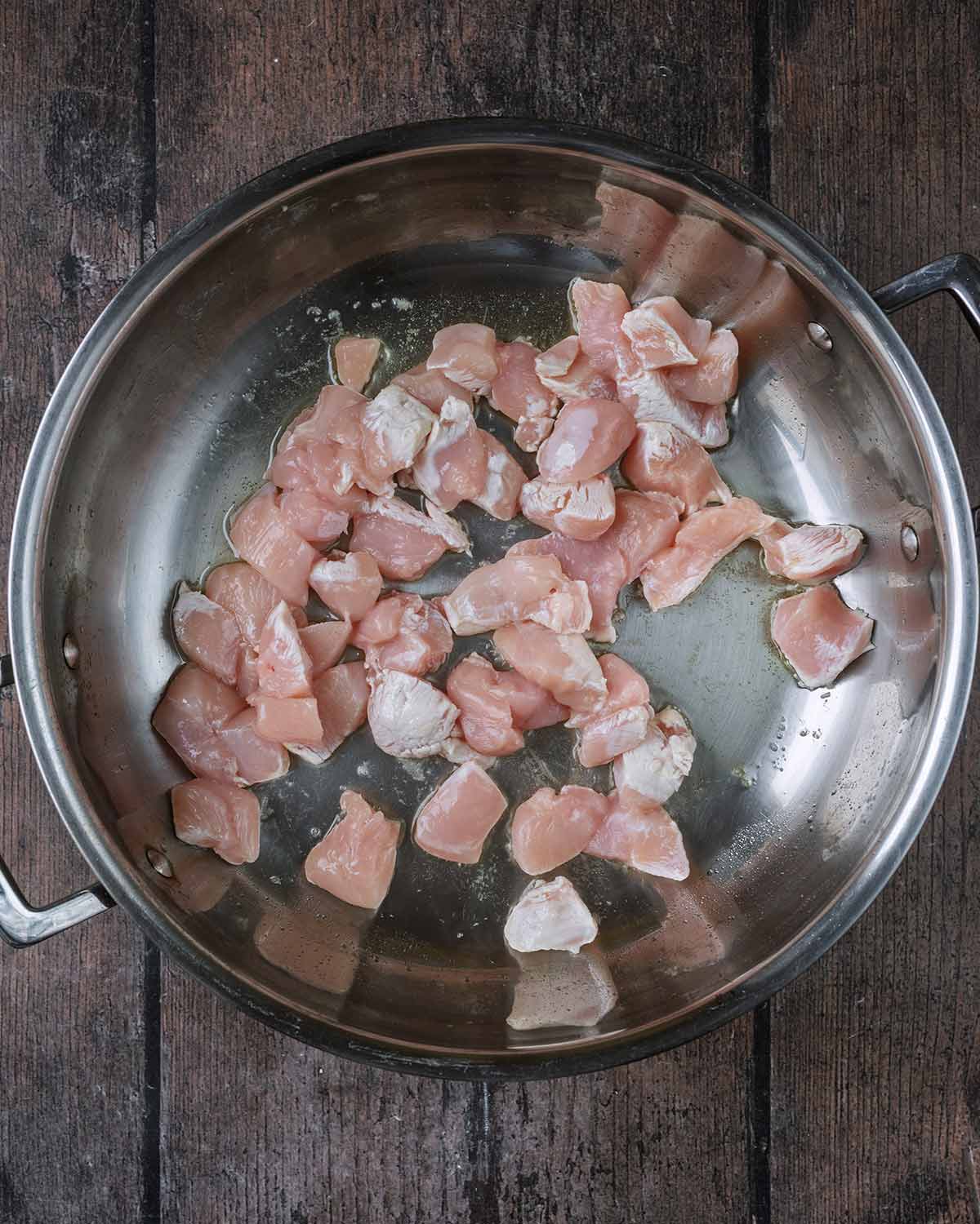 Chunks of chicken breast cooking in a large pan.