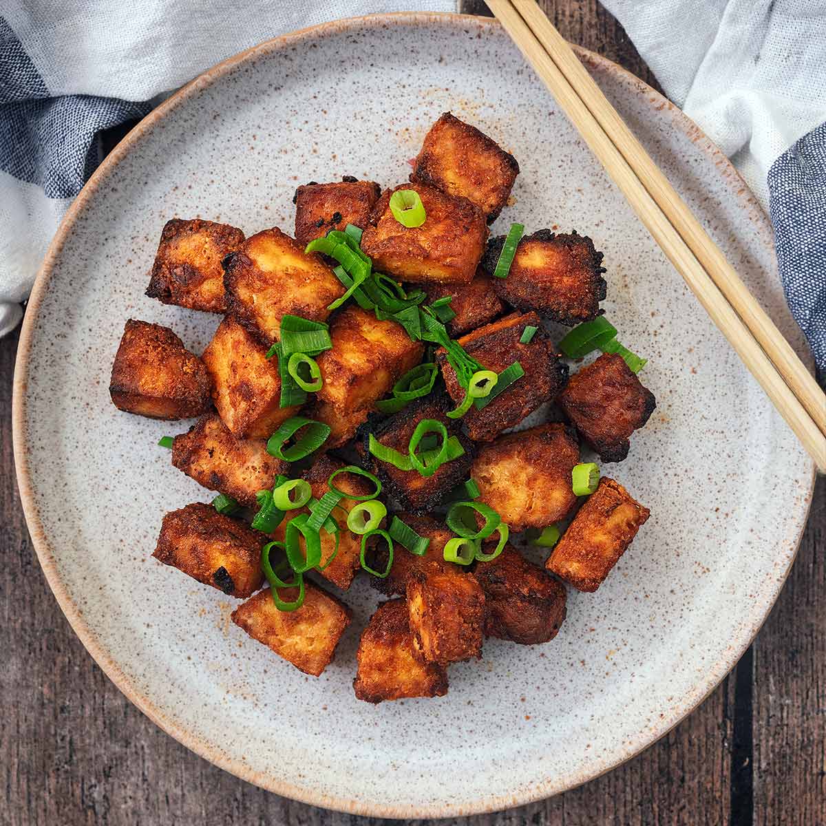 A plate of crispy baked tofu with a pair of chopsticks.