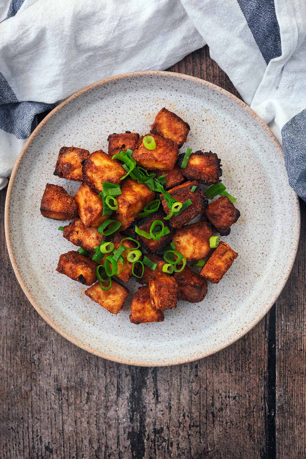 A plate of crispy tofu cubes next to a striped towel.