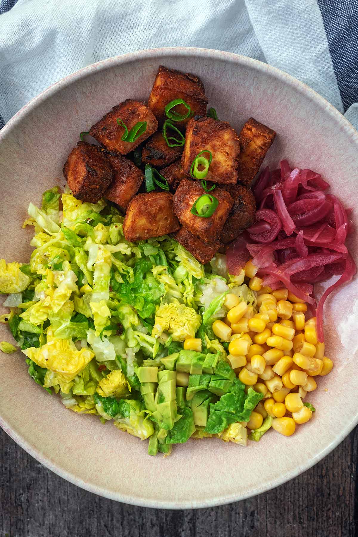 Crispy tofu bites in a bowl with lettuce, corn and pickled red onions.