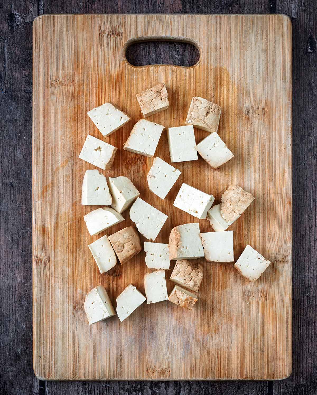 Cubes of tofu on a wooden chopping board.