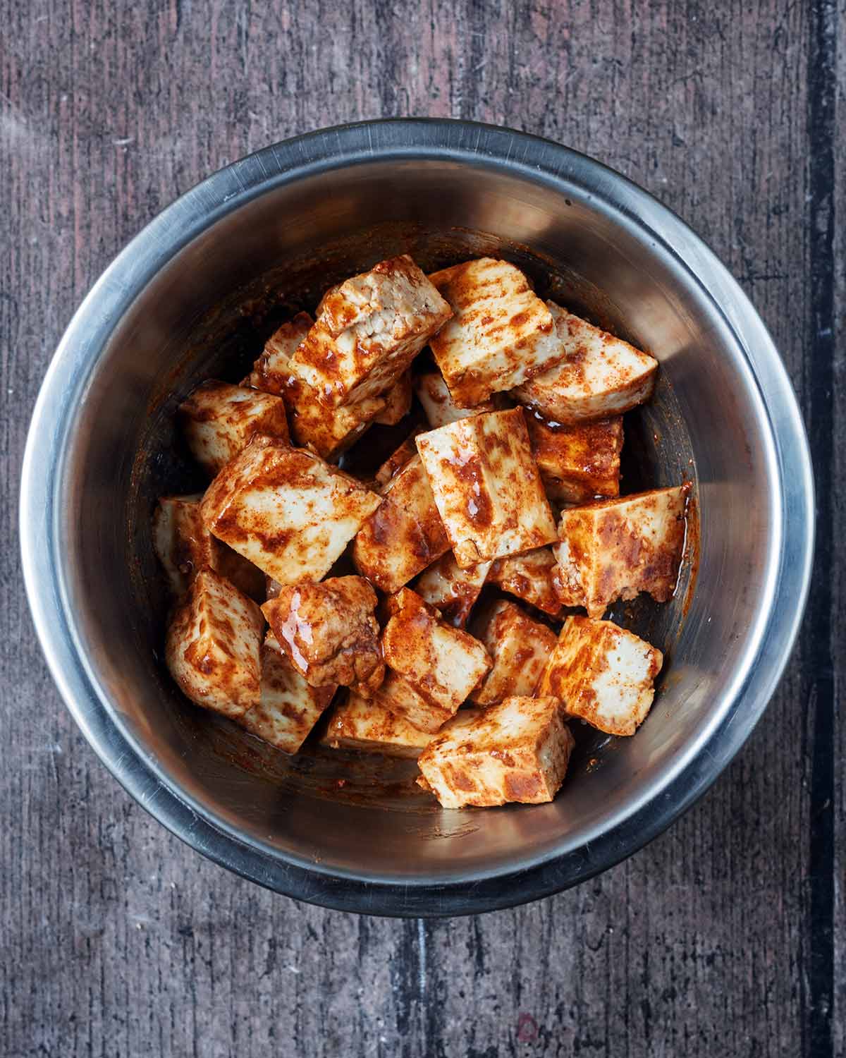 Cubes of tofu in a bowl with soy sauce, oil, paprika and garlic granules.