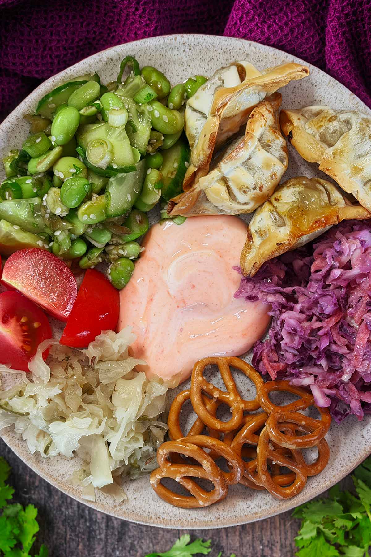 A picky plate of gyoza, edamame salad, tomatoes, onions, pretzels, sauerkraut and sauce.