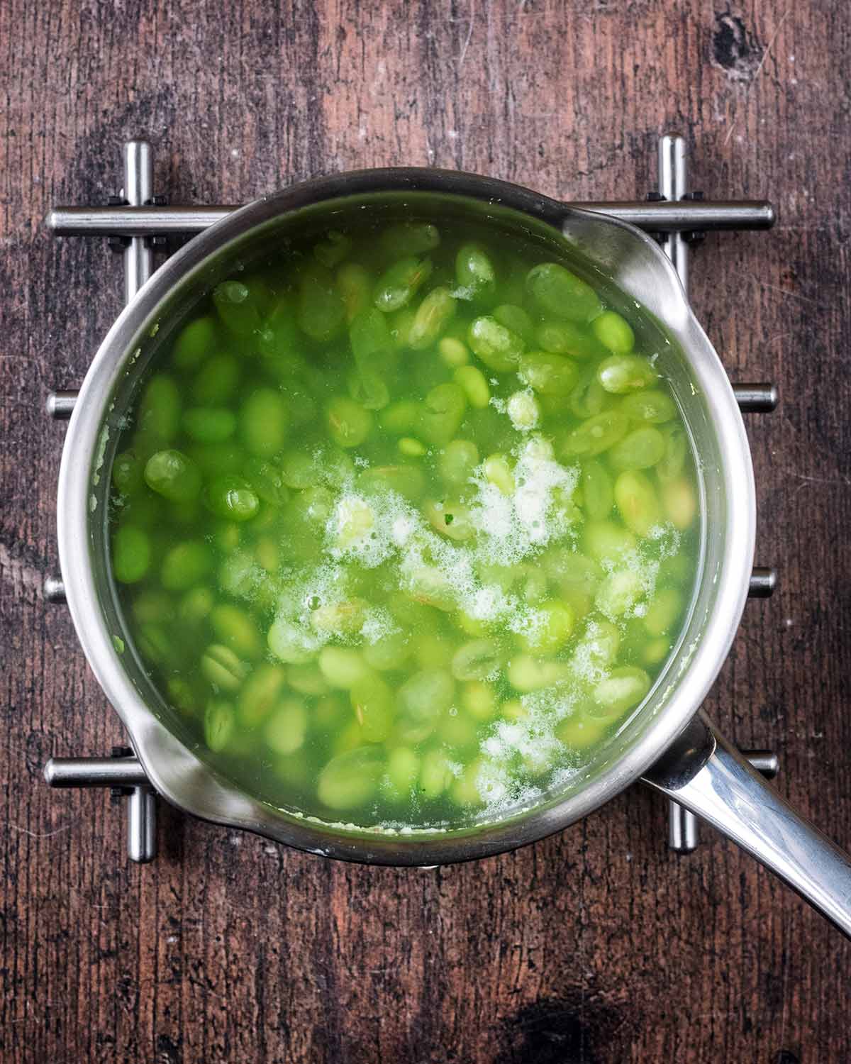 A pan of edamame beans in boiling water.