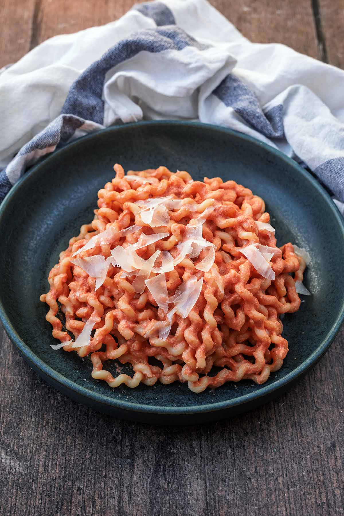 A bowl of pasta in a tomato sauce in front of a striped towel.