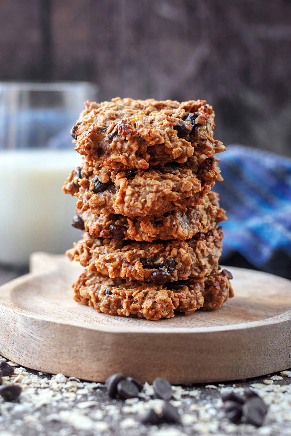 Five oat cookie stacked up on a small wooden board.