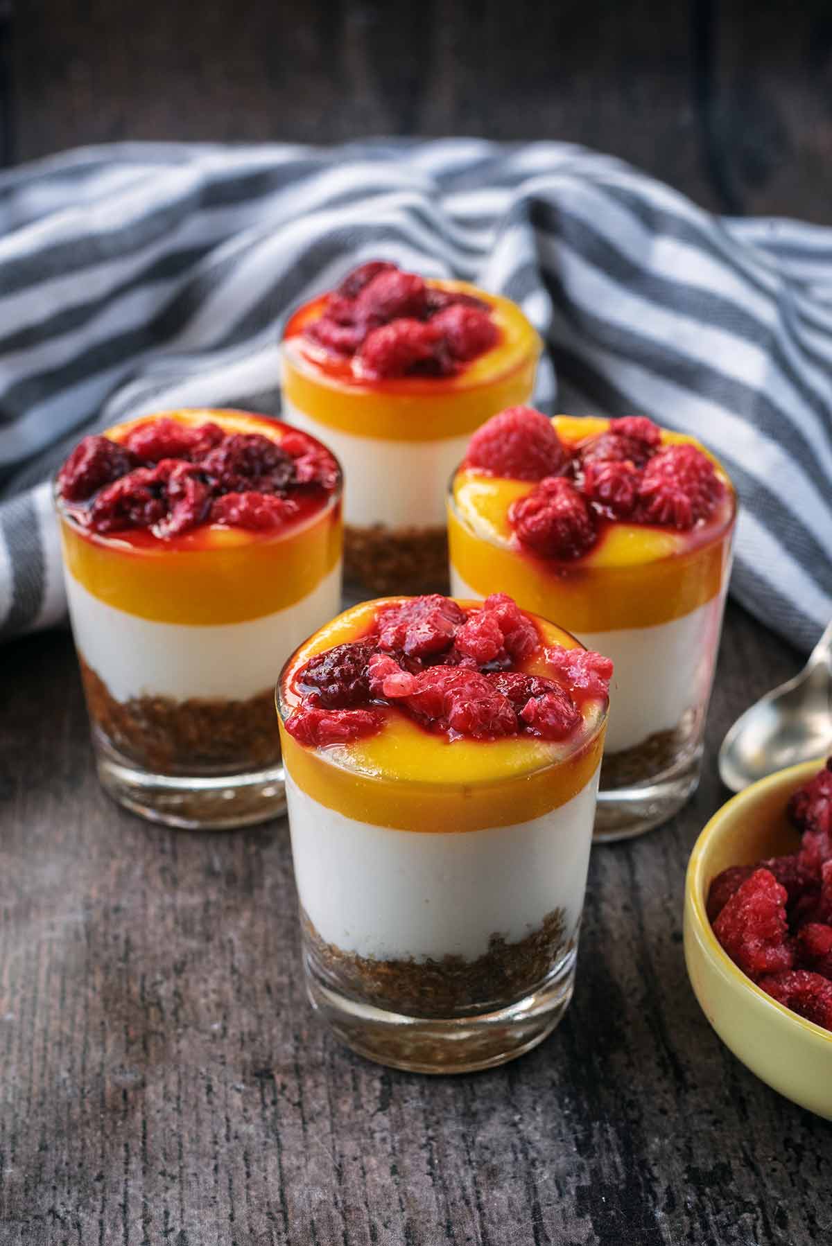 Four glasses of layered cheesecake in front of a striped towel.