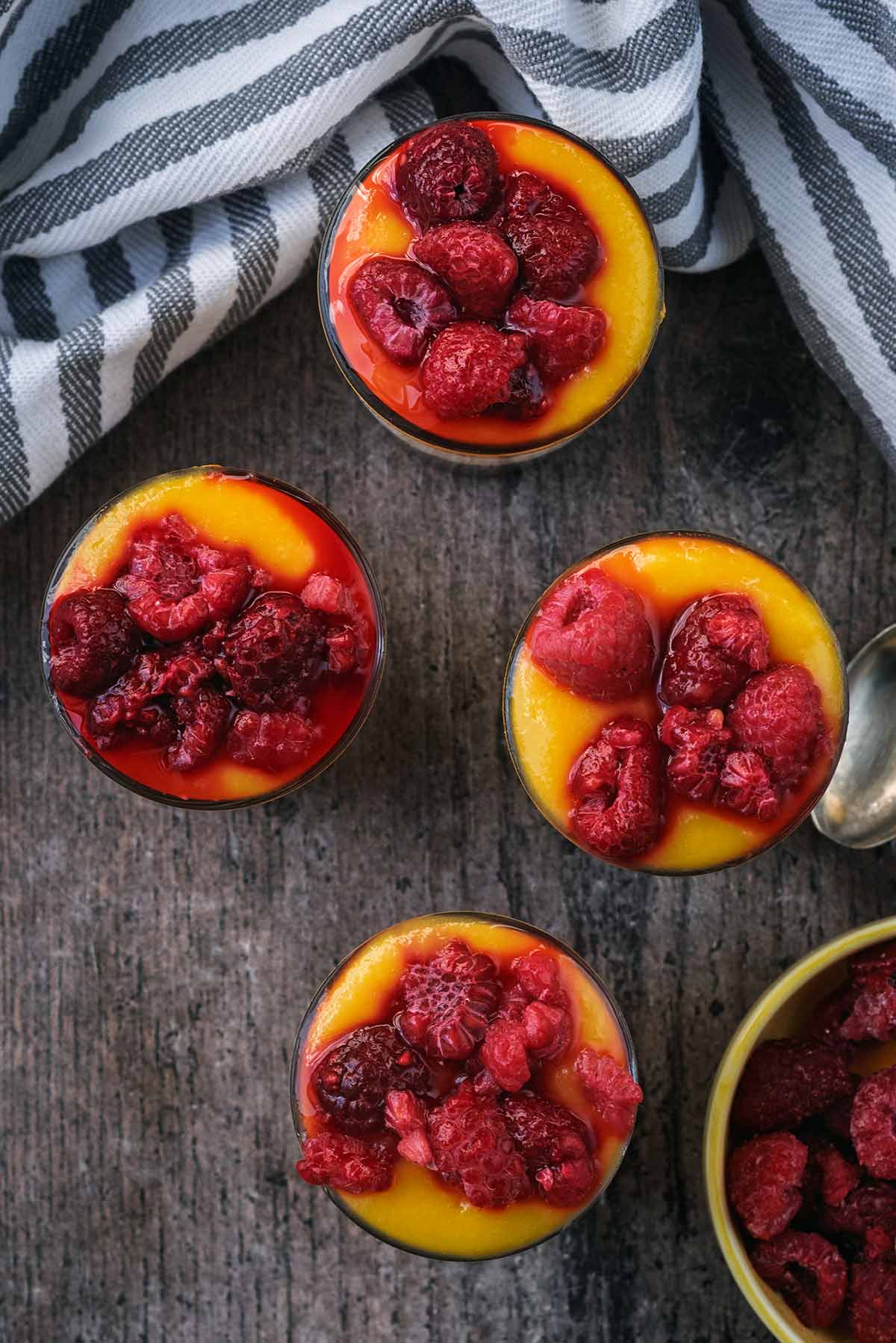 Four raspberry and mango topped cheesecakes as viewed from above.
