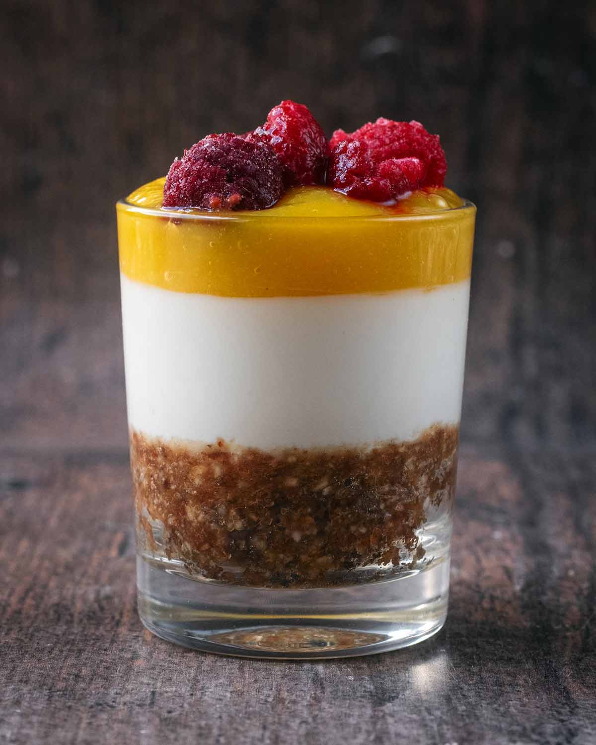 A layered cheesecake topped with mango puree and raspberries.