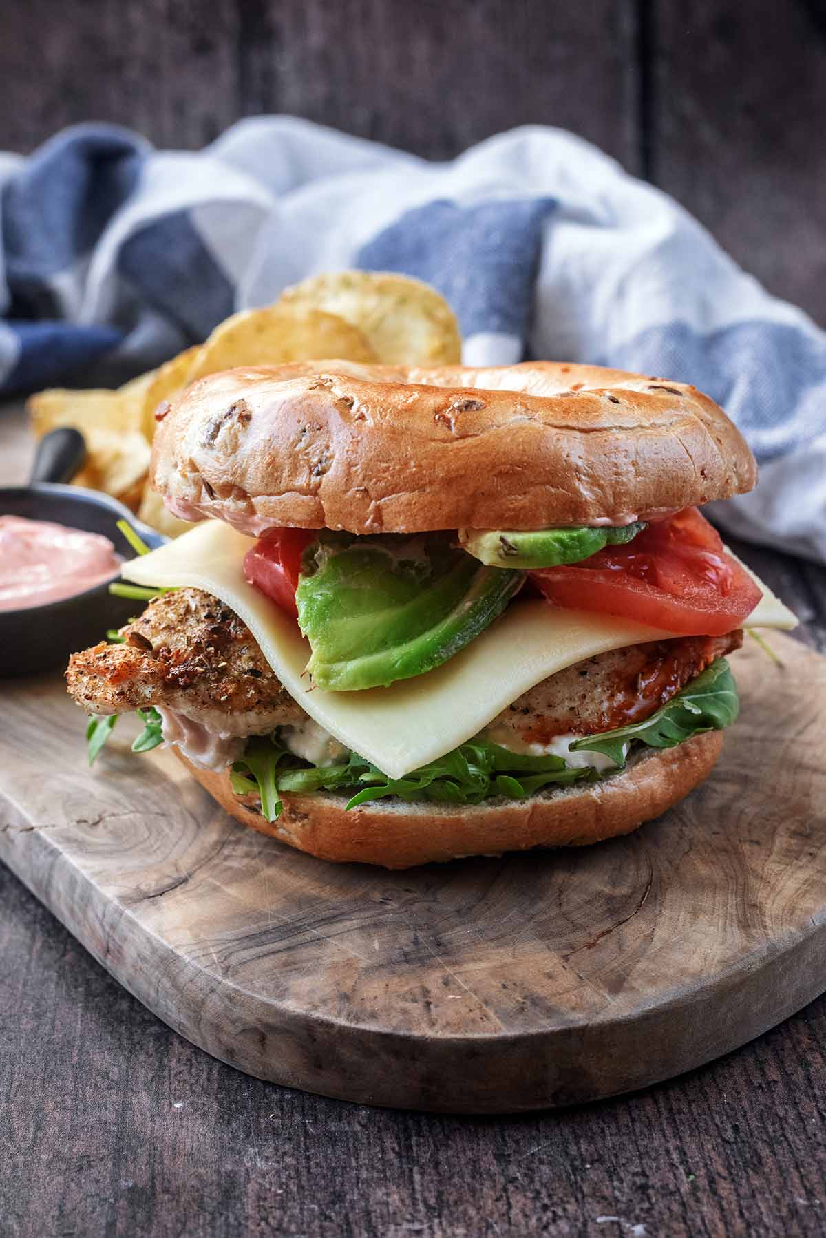 A bagel filled with lettuce, chicken breast, cheese, avocado and tomato.
