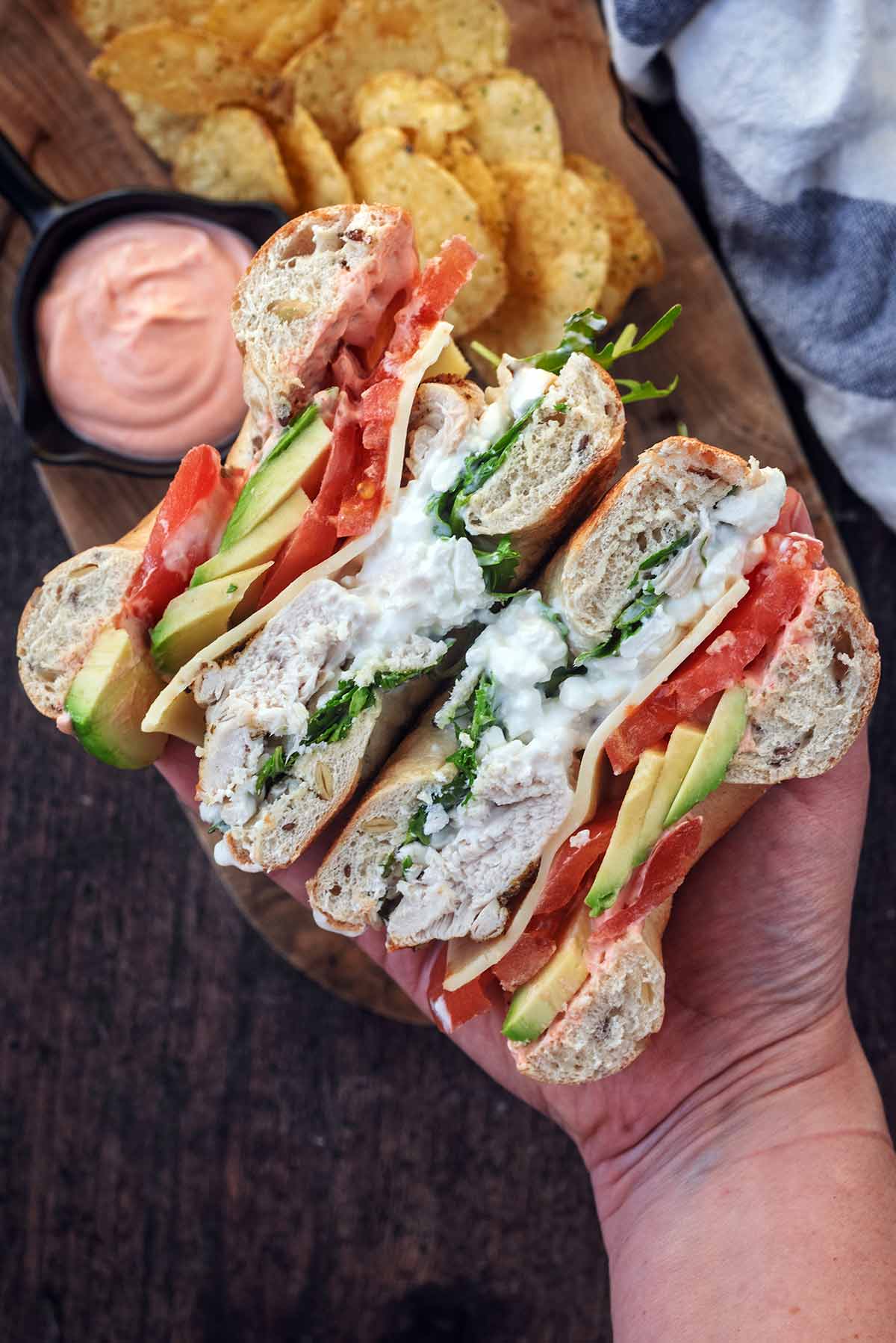A hand holding a filled bagel that has been sliced in half.