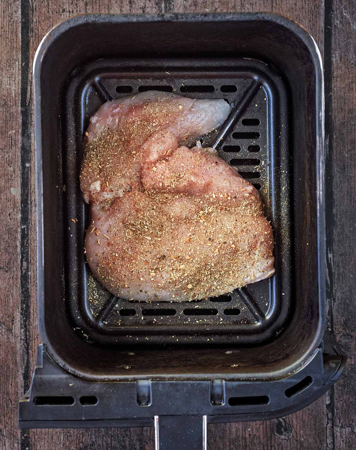A seasoned chicken breast in an air fryer basket.