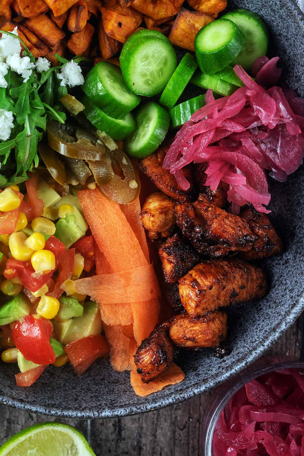 Cooked chicken, ribbons of carrot, sliced cucumber and sweetcorn salsa in a bowl.