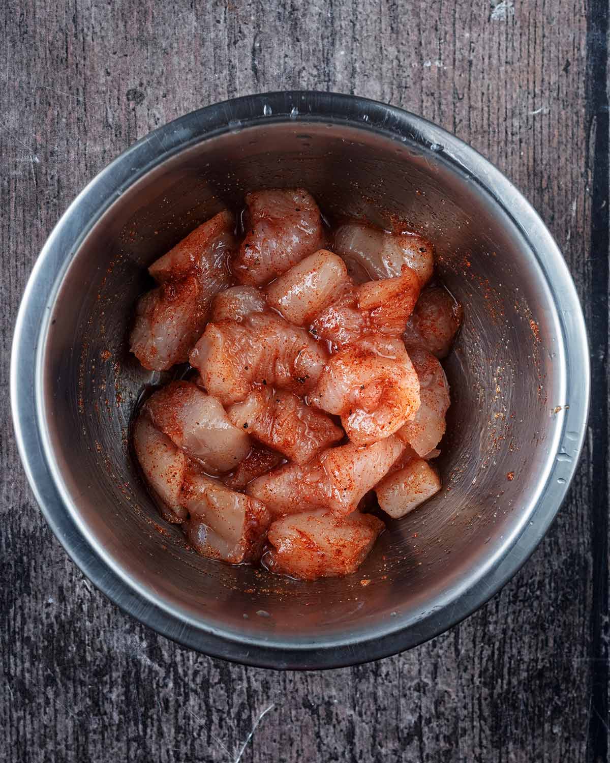 A bowl of diced chicken coated in oil and seasoning.