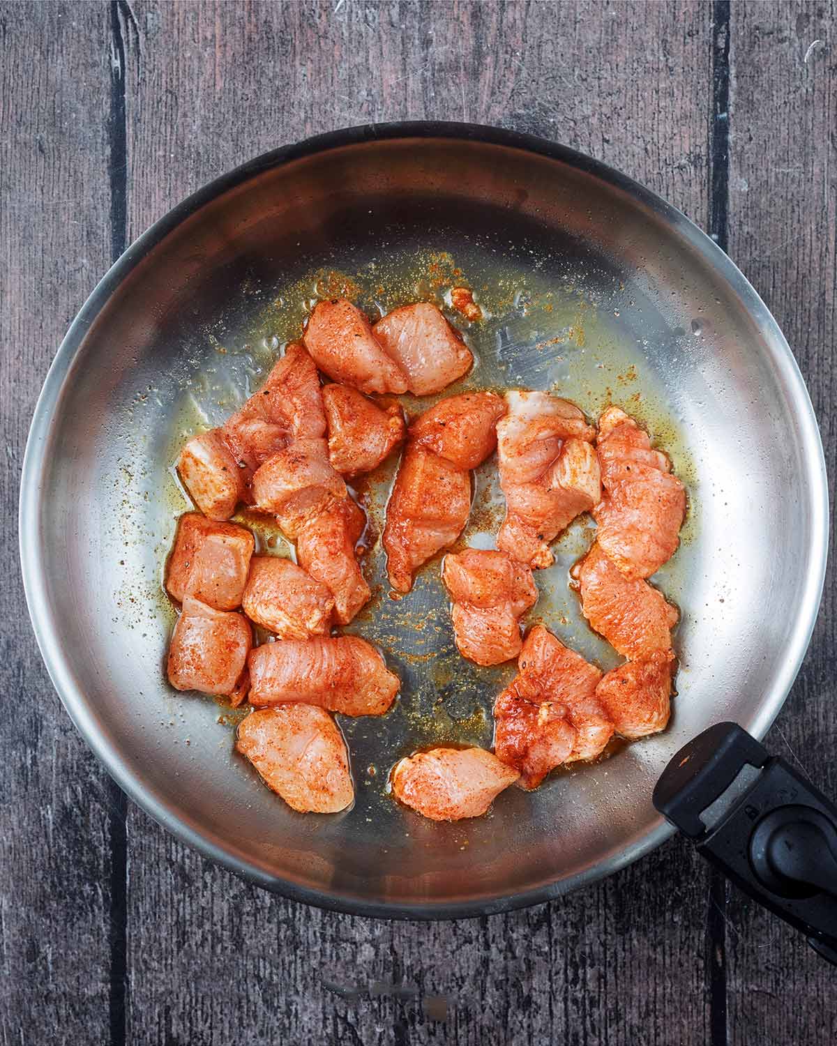 Seasoned chicken cubes frying in a large pan.
