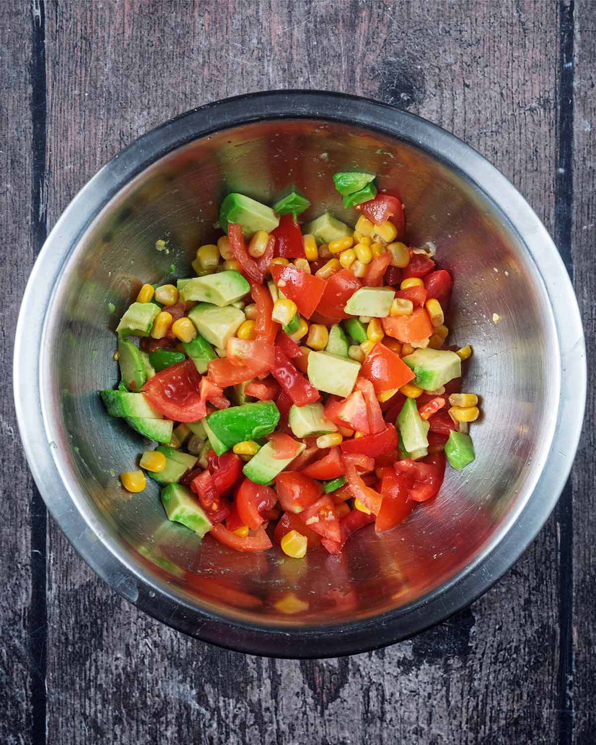 A mixing bowl containing chopped tomatoes, diced avocado and sweetcorn.