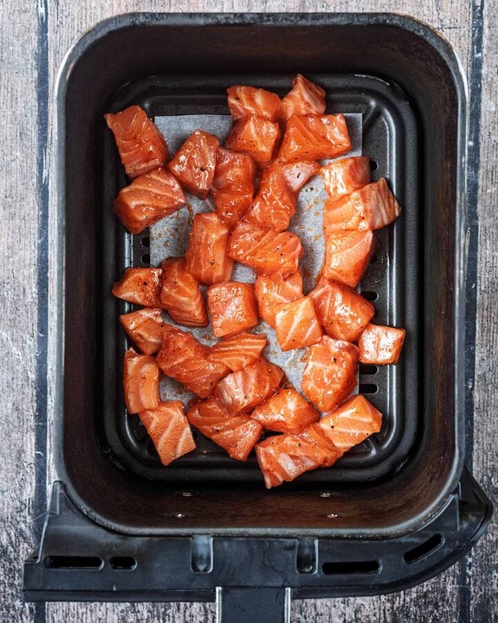 The coated salmon chunks in an air fryer basket.