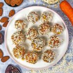 Twelve raw carrot cake bites on a small round plate.