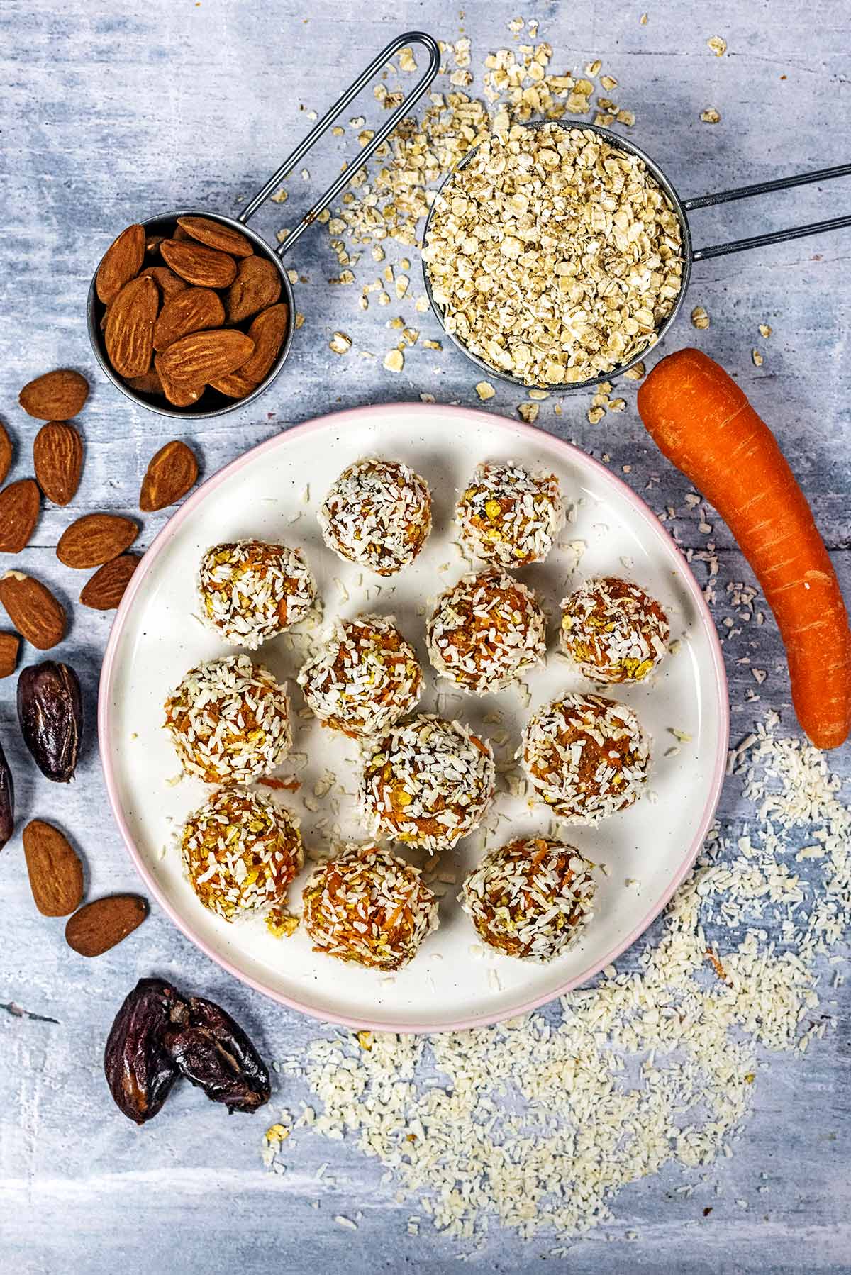 Twelve carrot cake bites surrounded by nuts, oats, dates and a carrot.