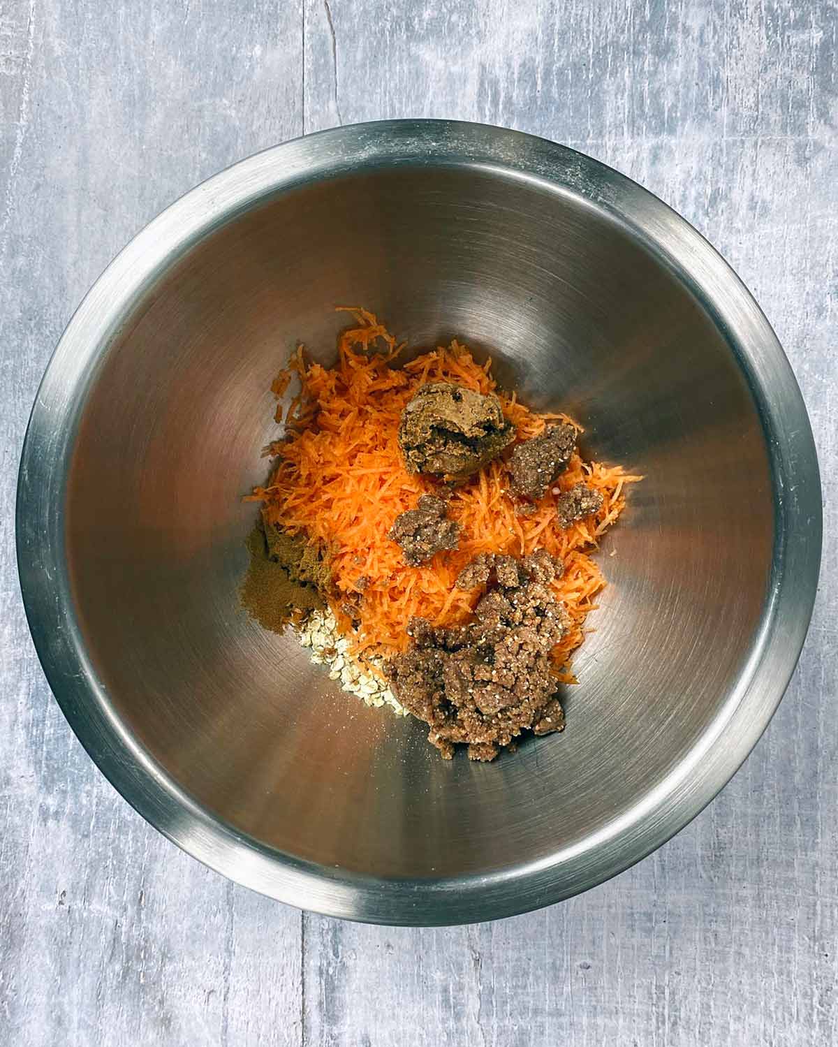 Date paste, grated carrot, nut butter, oats and cinnamon in a mixing bowl.