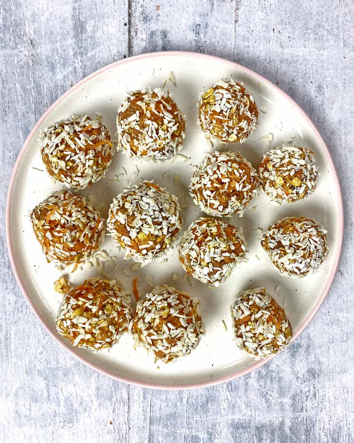 Twelve cake balls on a plate, each rolled in desiccated coconut.