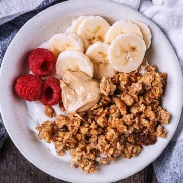 A bowl of scrambled oats, banana slices, raspberries and yogurt.